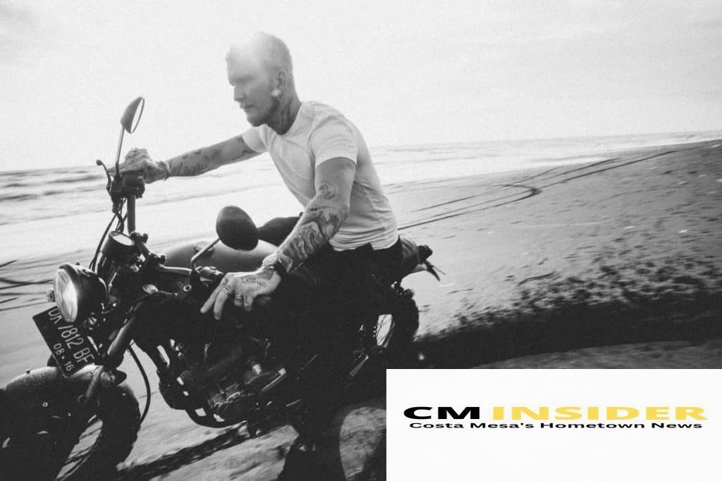 tattooed motorcyclist riding bike on sandy beach near ocean