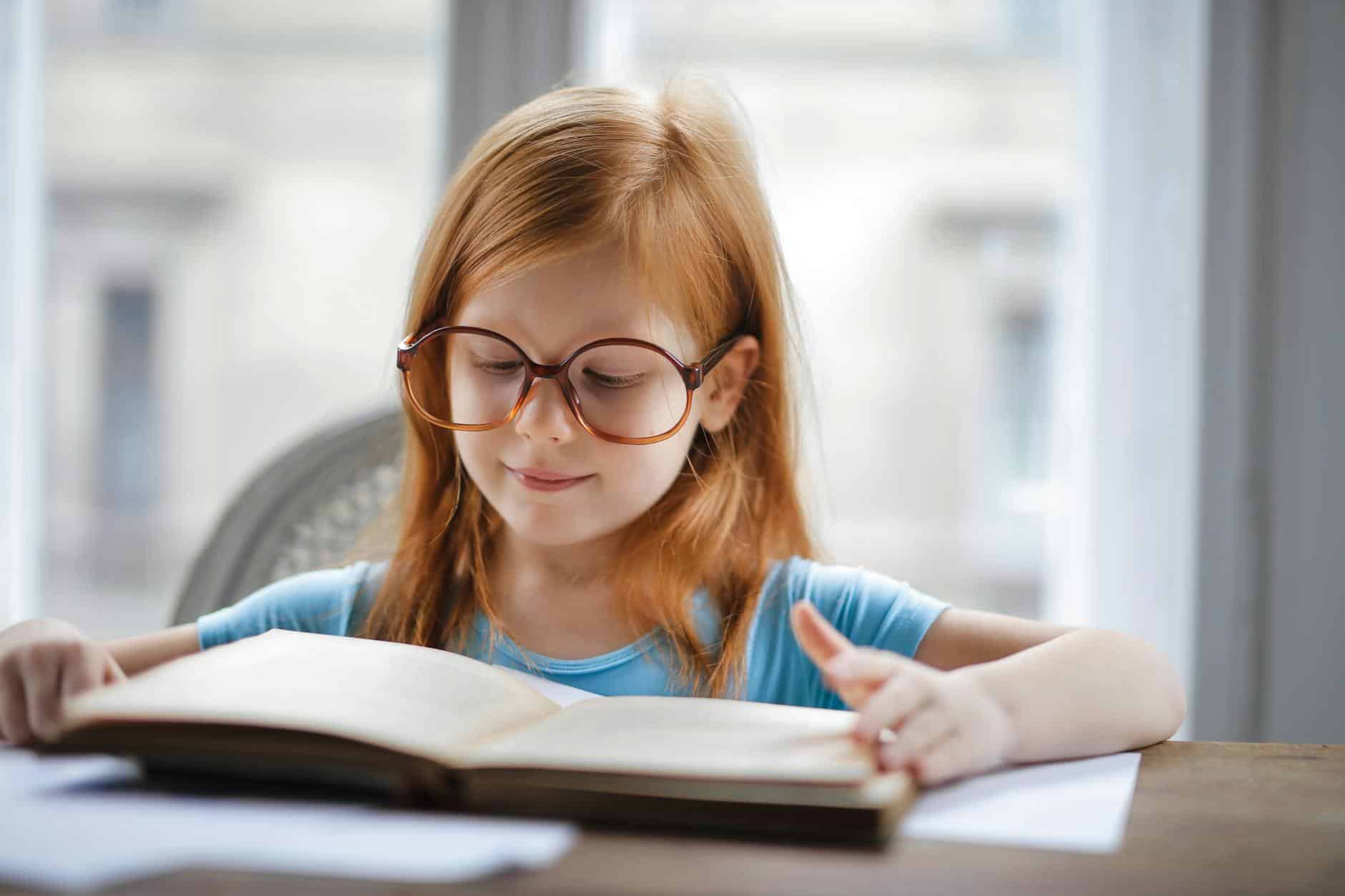 girl in blue shirt wearing eyeglasses reading book